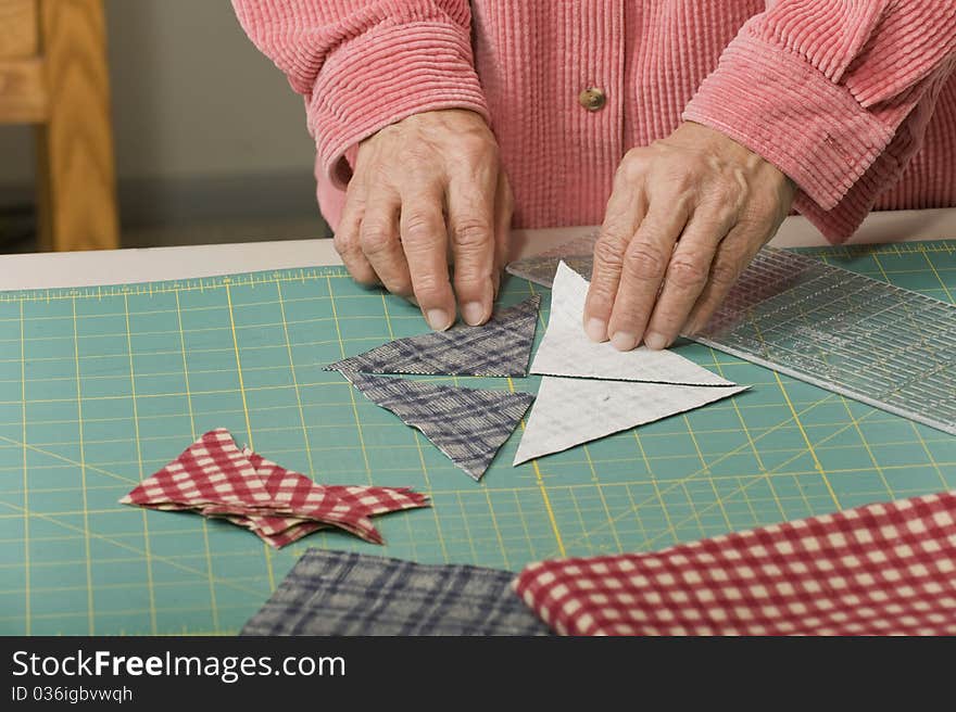 A woman positions four triangle pieces of fabric to make a quilt square. A woman positions four triangle pieces of fabric to make a quilt square.