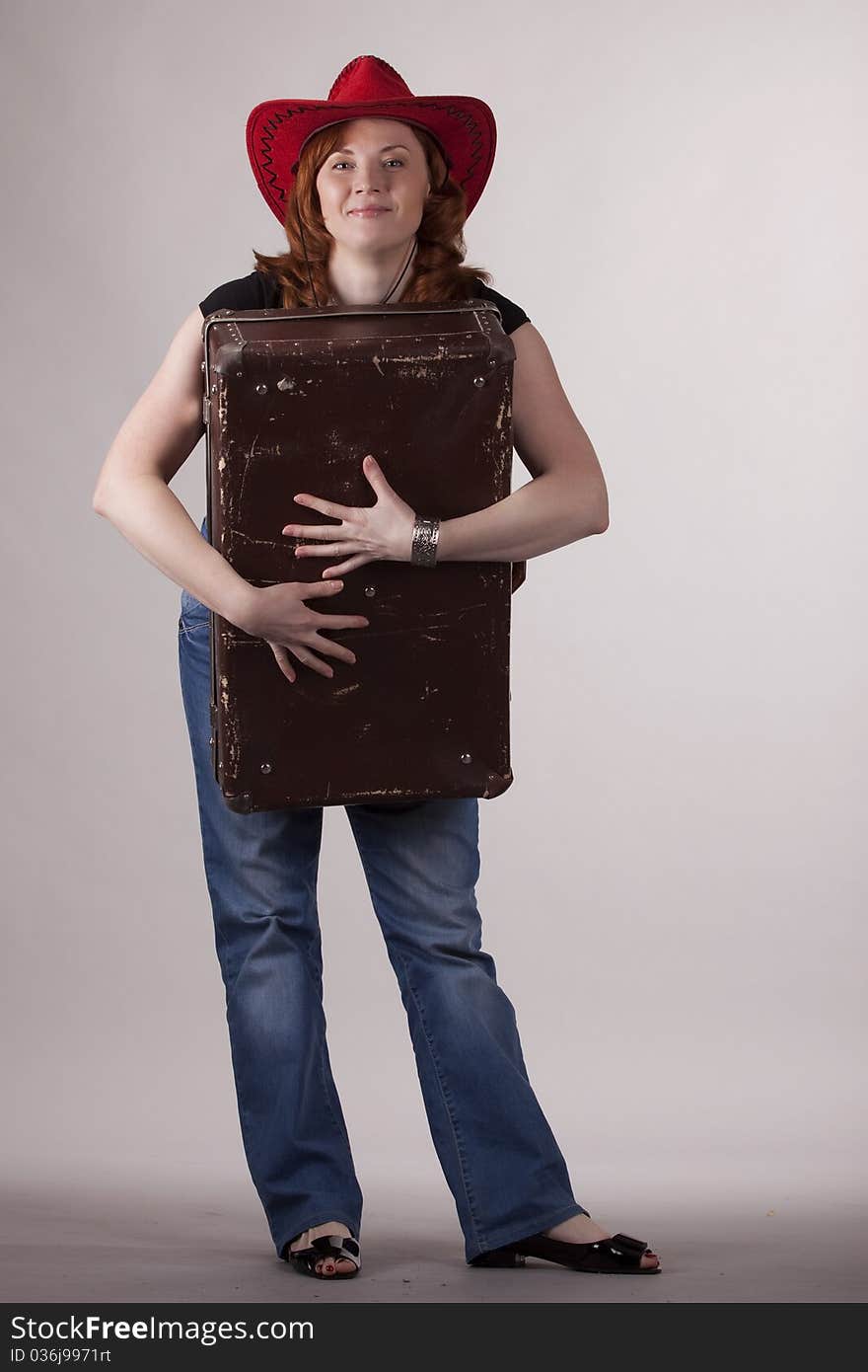 The girl in a red hat with old suitcases in hands on a gray background. The girl in a red hat with old suitcases in hands on a gray background