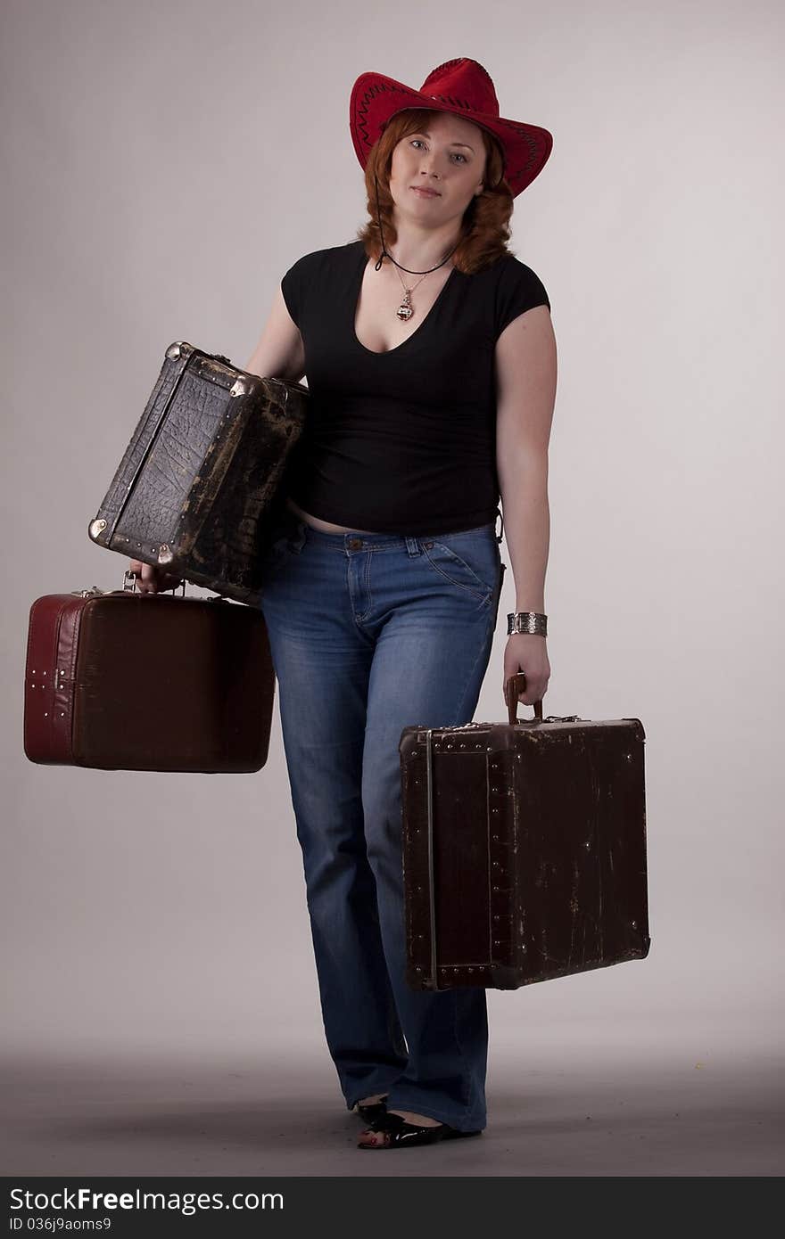 The girl in a red hat with old suitcases in hands on a gray background. The girl in a red hat with old suitcases in hands on a gray background