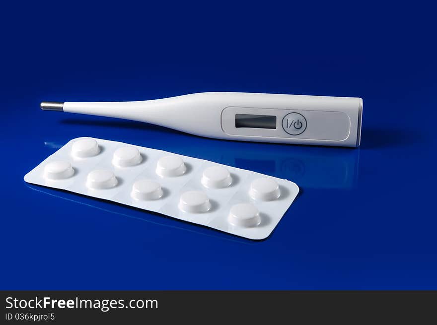 Tablets and thermometer on a blue background