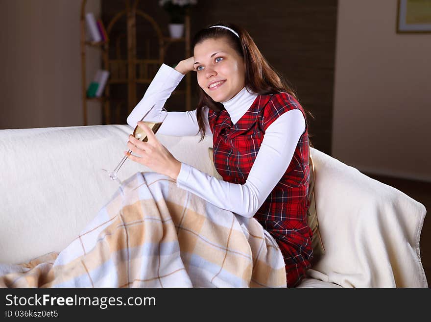 A young girl sitting on the sofa at home with a glass of wine. A young girl sitting on the sofa at home with a glass of wine