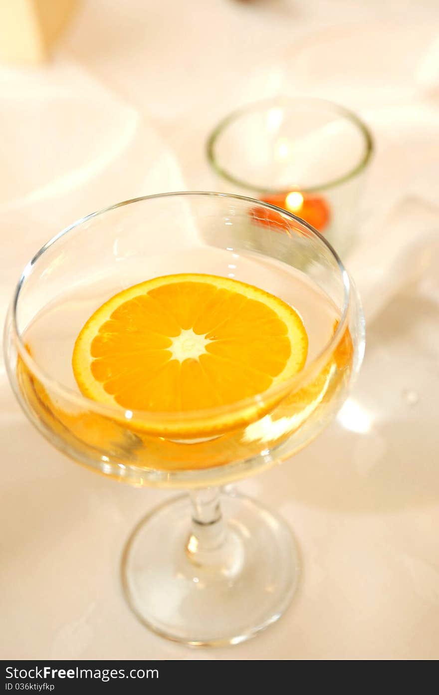 Detail of a glass with a slice of orange and a candle in background