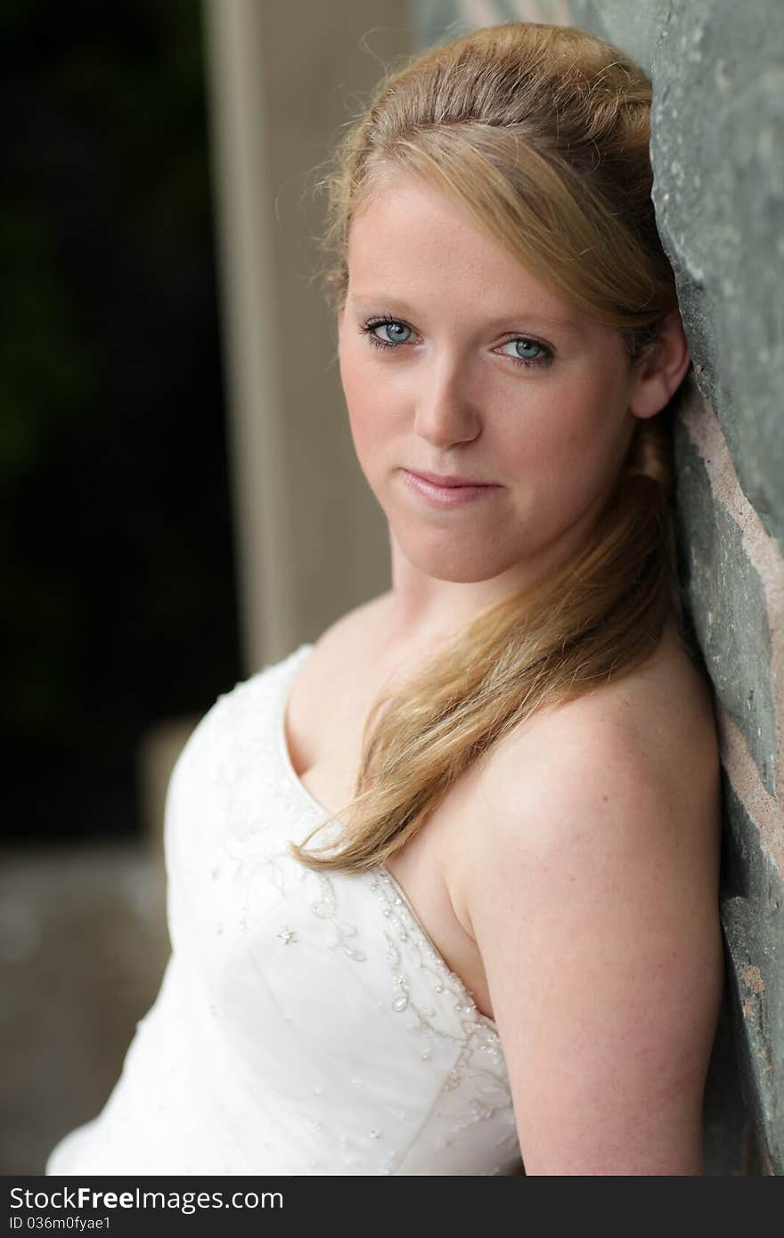 Bride in wedding dress leaning against a rock wall. Bride in wedding dress leaning against a rock wall