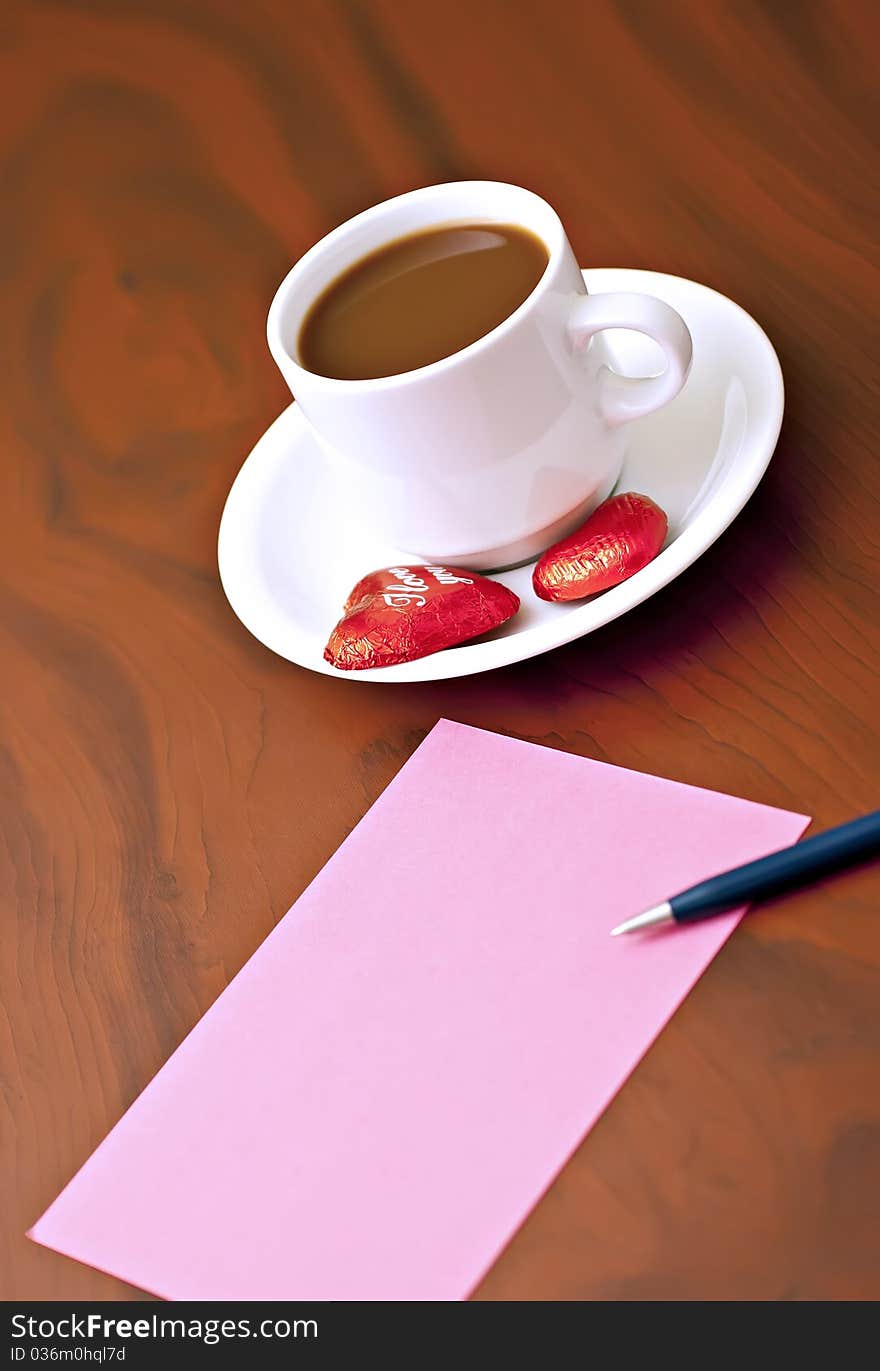 Coffee cup on the table with chocolates, a pink card and a pen. Coffee cup on the table with chocolates, a pink card and a pen.