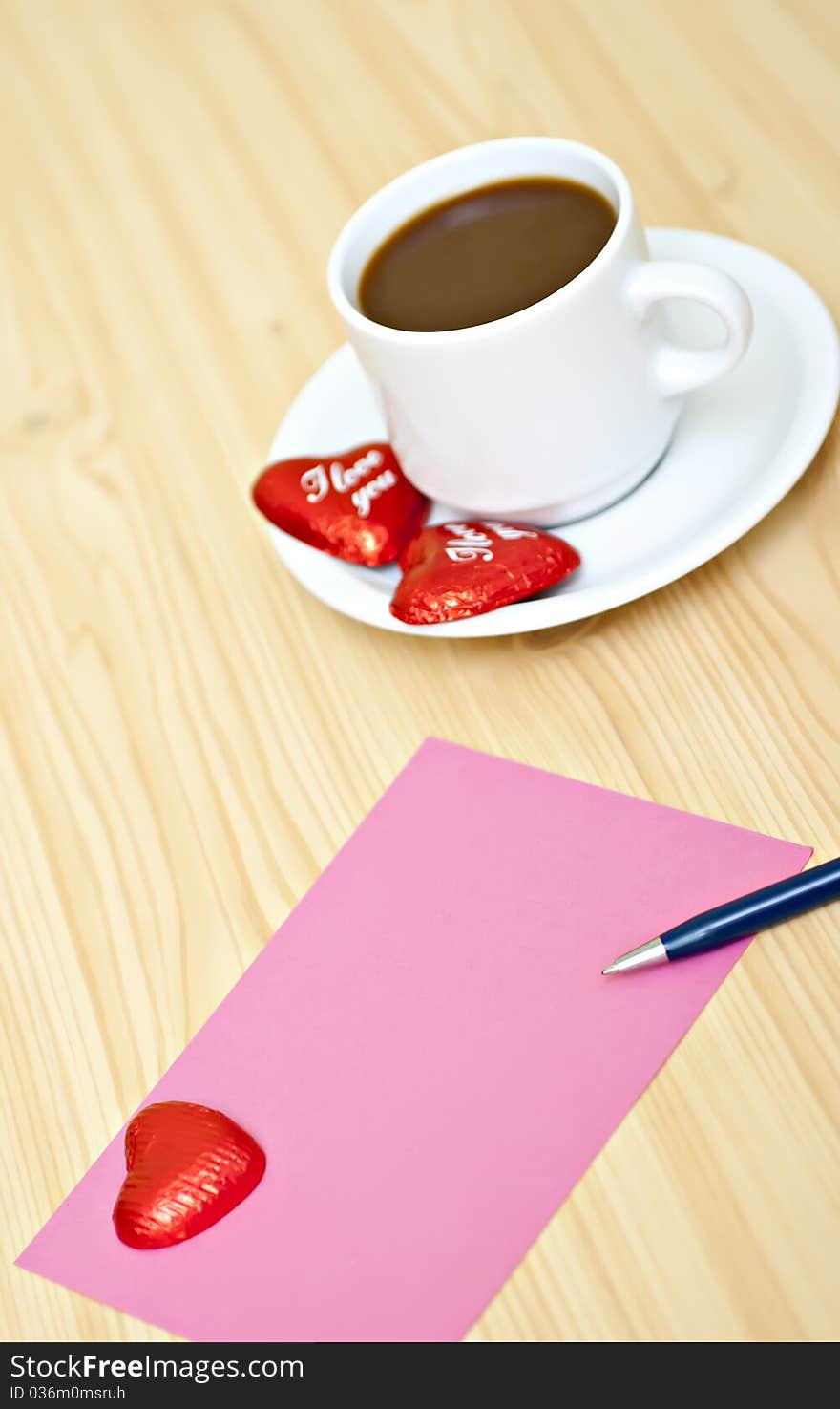 Coffee cup on the table with chocolates, a pink card and a pen. Coffee cup on the table with chocolates, a pink card and a pen.