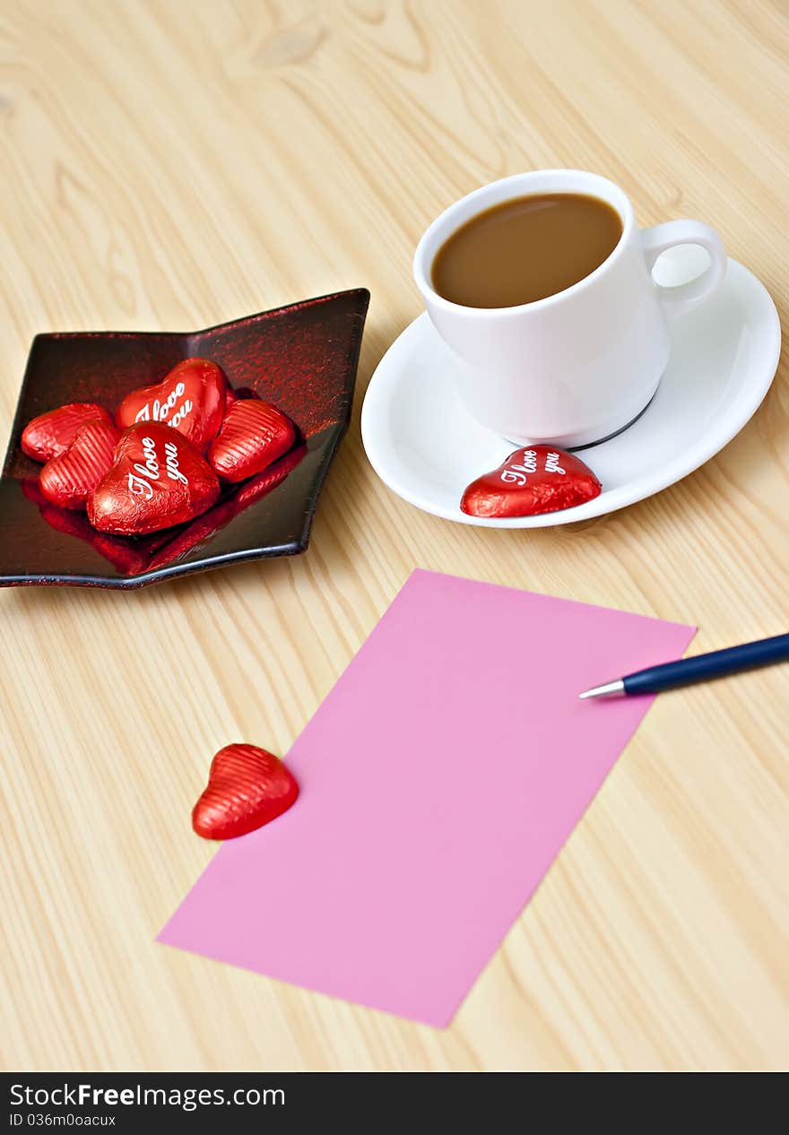 Coffee cup on the table with chocolates, a pink card and a pen. Coffee cup on the table with chocolates, a pink card and a pen.