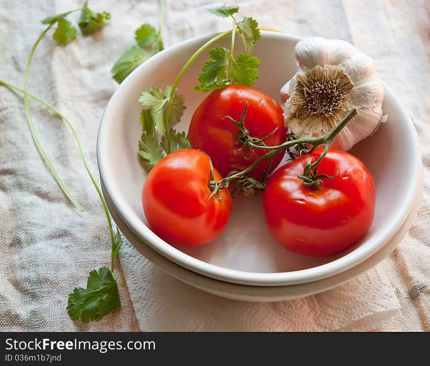 Tomatoes and garlic on a white plate in a rustic setting. Tomatoes and garlic on a white plate in a rustic setting