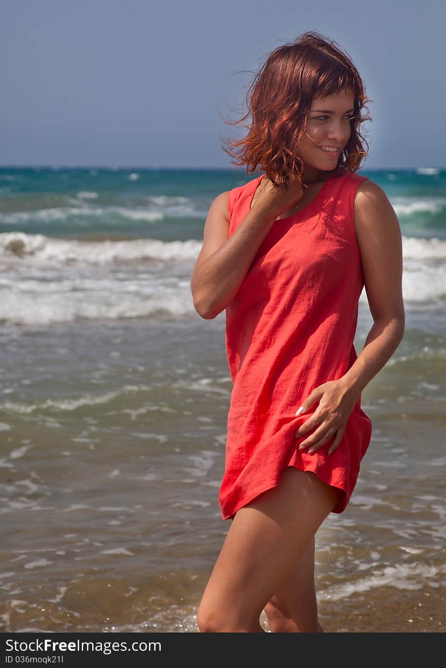 A beautiful smiling girl in red dress is on the beach. A beautiful smiling girl in red dress is on the beach