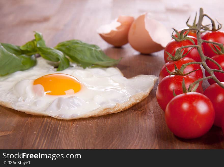 Fried egg served on a wooden table with tomato and fresh herbs. Fried egg served on a wooden table with tomato and fresh herbs