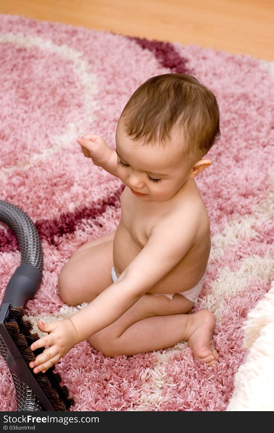 Cute caucasian baby with vacuum cleaner on the carpet