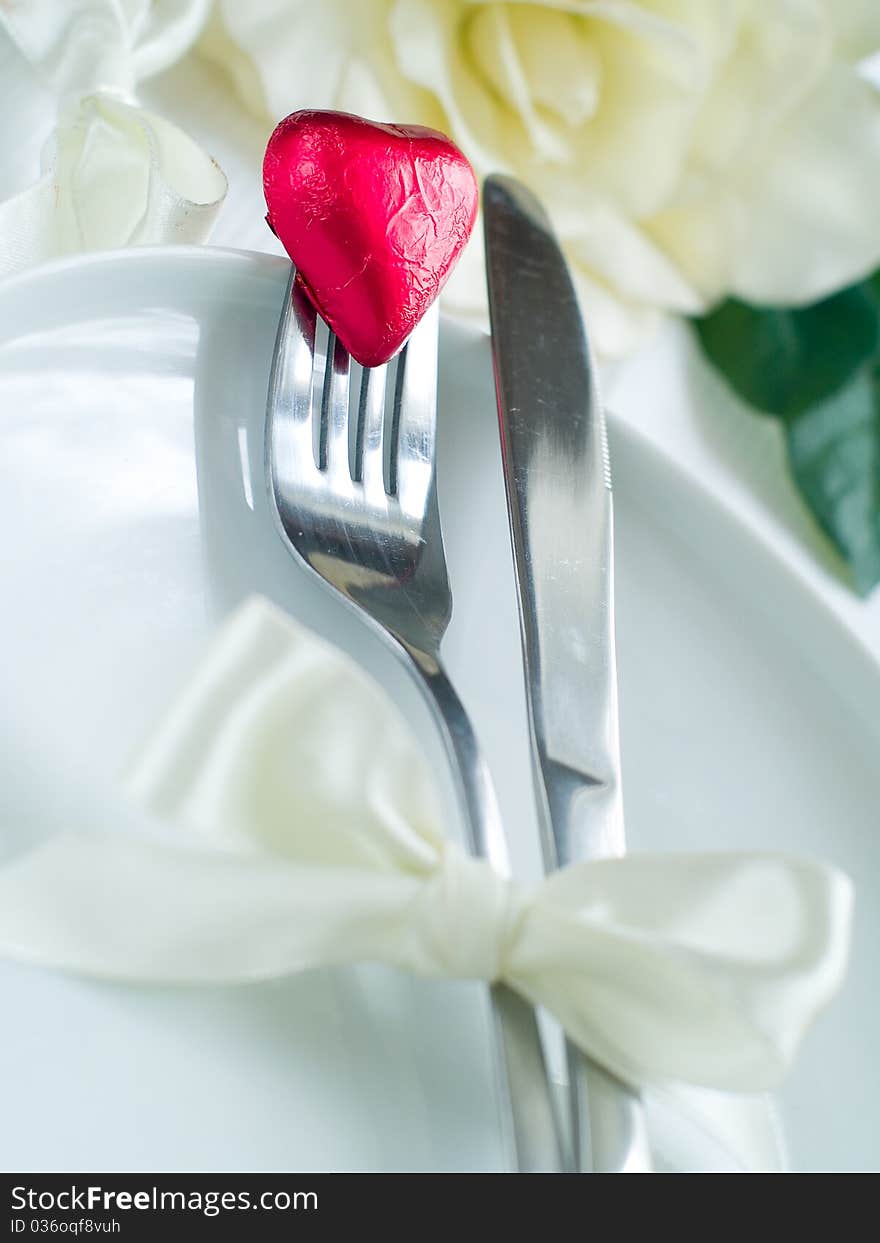 Fork and knife laying on plate with ribbon and heart. Fork and knife laying on plate with ribbon and heart