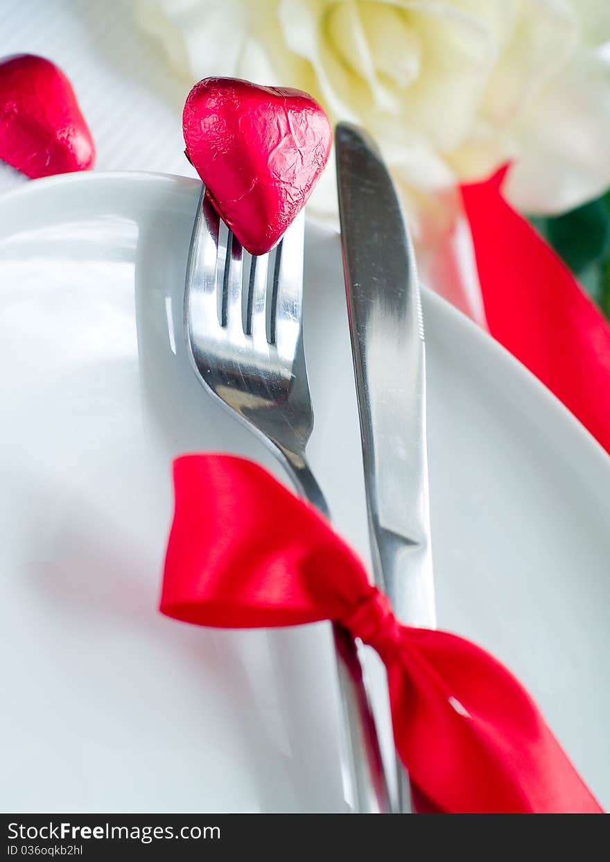 Fork and knife laying on plate with ribbon and heart. Fork and knife laying on plate with ribbon and heart