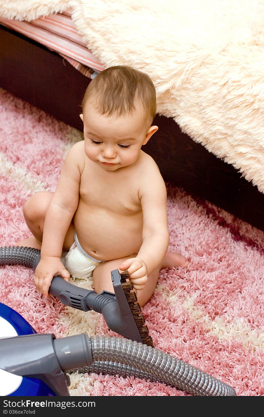 Cute caucasian baby with vacuum cleaner on the carpet