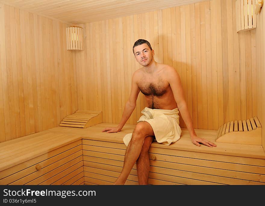 Young handsome man in a towel relaxing in a russian wooden sauna. Young handsome man in a towel relaxing in a russian wooden sauna