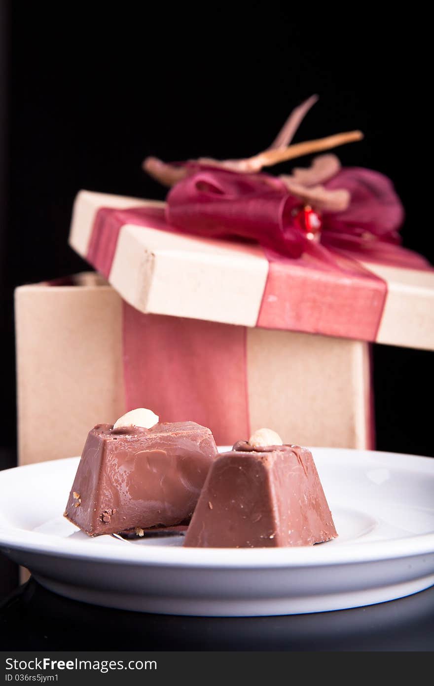 Two chocolate on a plate with gift box on dark background