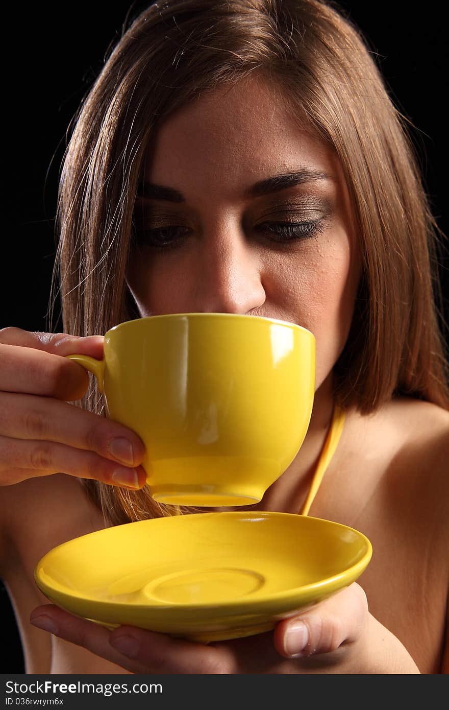 Portrait of a beautiful young caucasion woman drinking tea from a yellow cup and saucer. Portrait of a beautiful young caucasion woman drinking tea from a yellow cup and saucer.