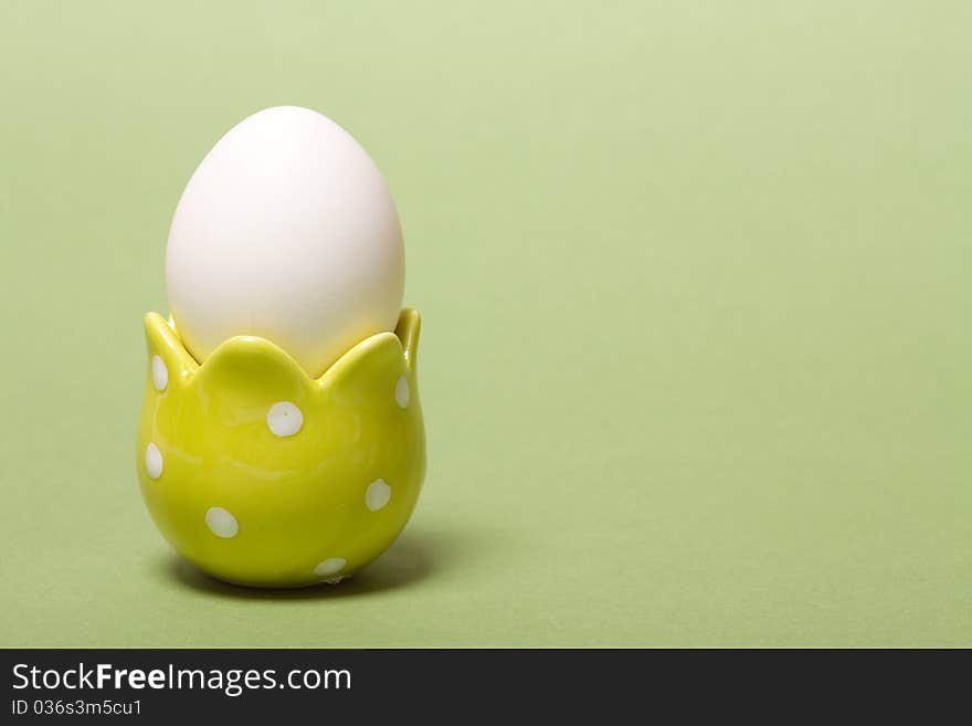 White easter eggs in yellow  eggcup on green background