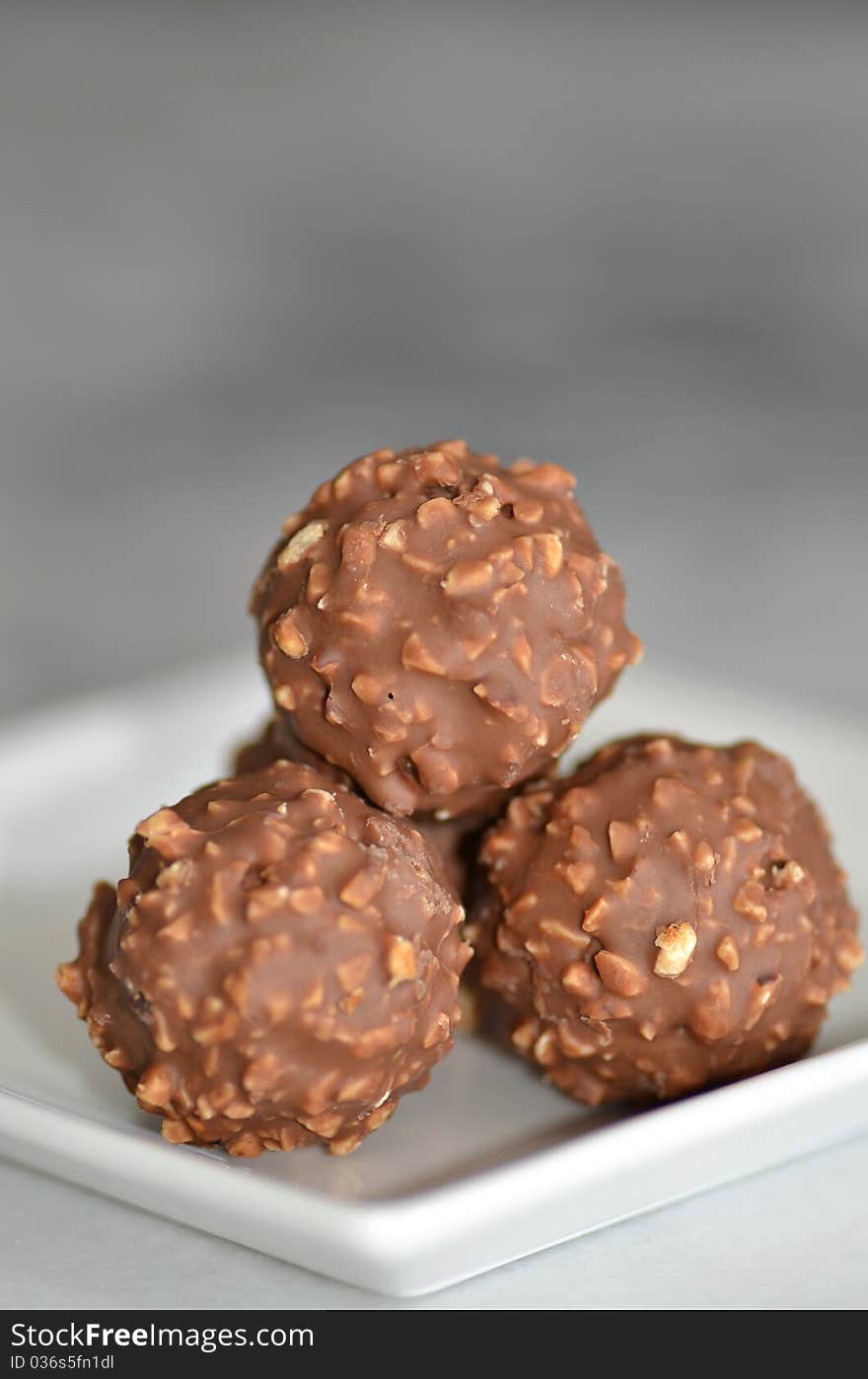 Nut coated chocolates served on a white plate.