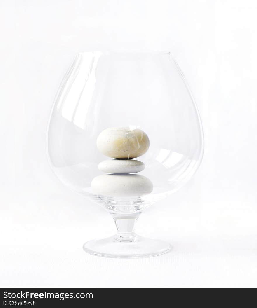 This is photo of big transparent glass with three pebbles on white background. This is photo of big transparent glass with three pebbles on white background.