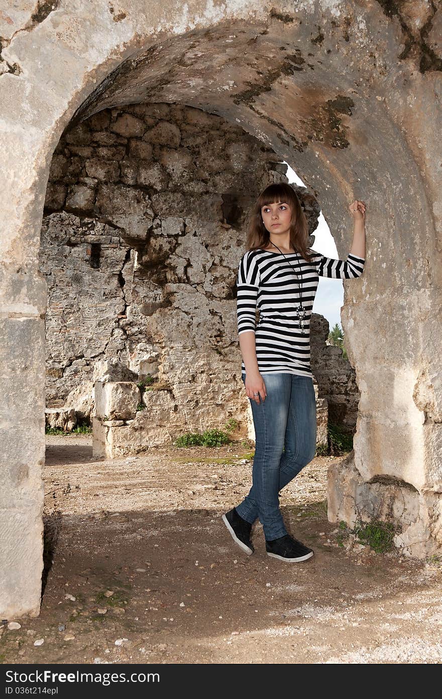 Young girl in jeans in an arch in the ruins