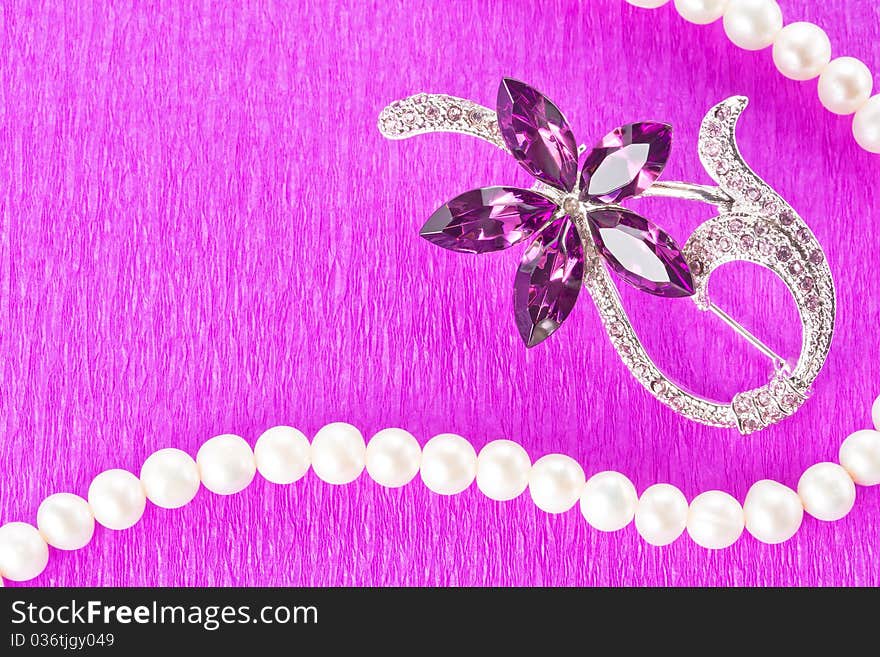 Brooch and pearl necklace on purple background as decorative frame