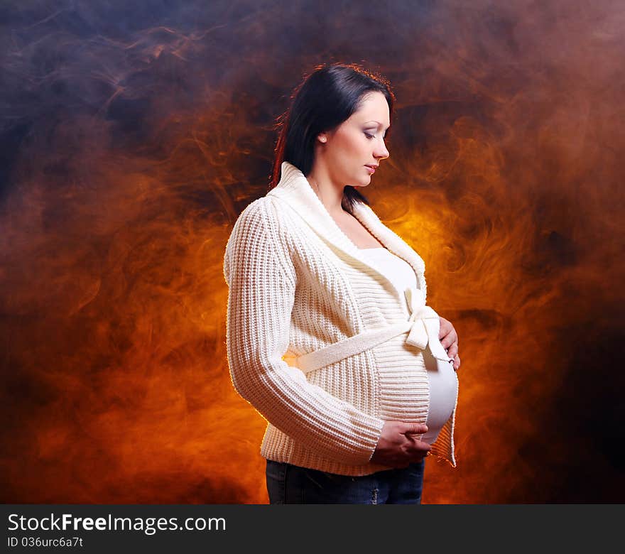 Young and beautiful pregnant woman on black background with smoke