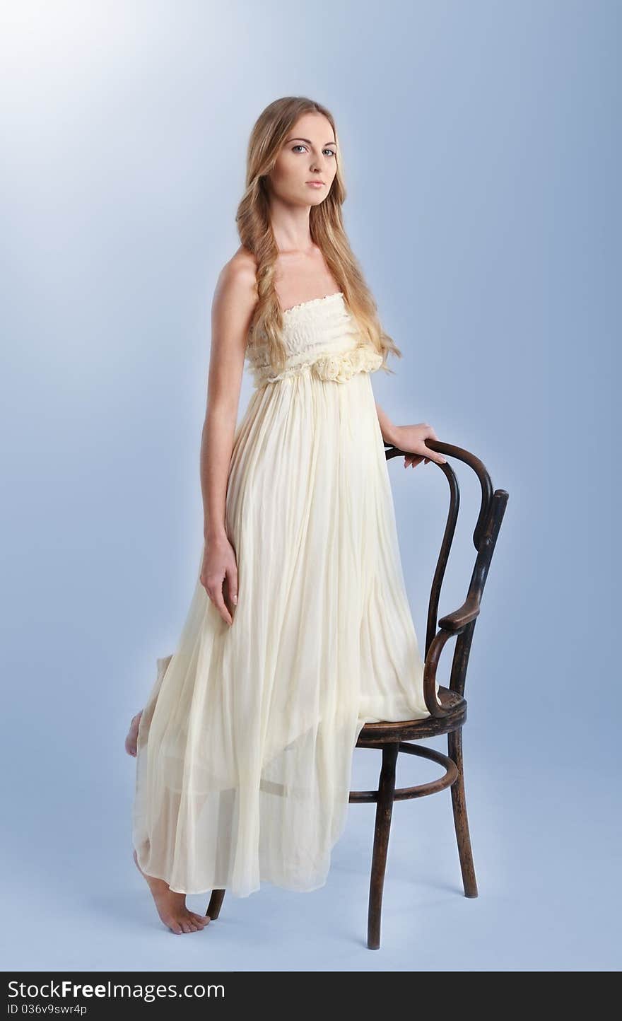 Young fashionable blond girl in long dress near the chair