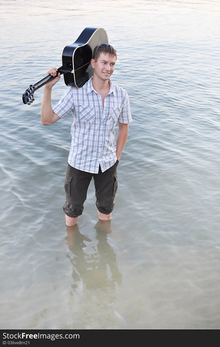 A young man stands in water with a black guitar. A young man stands in water with a black guitar