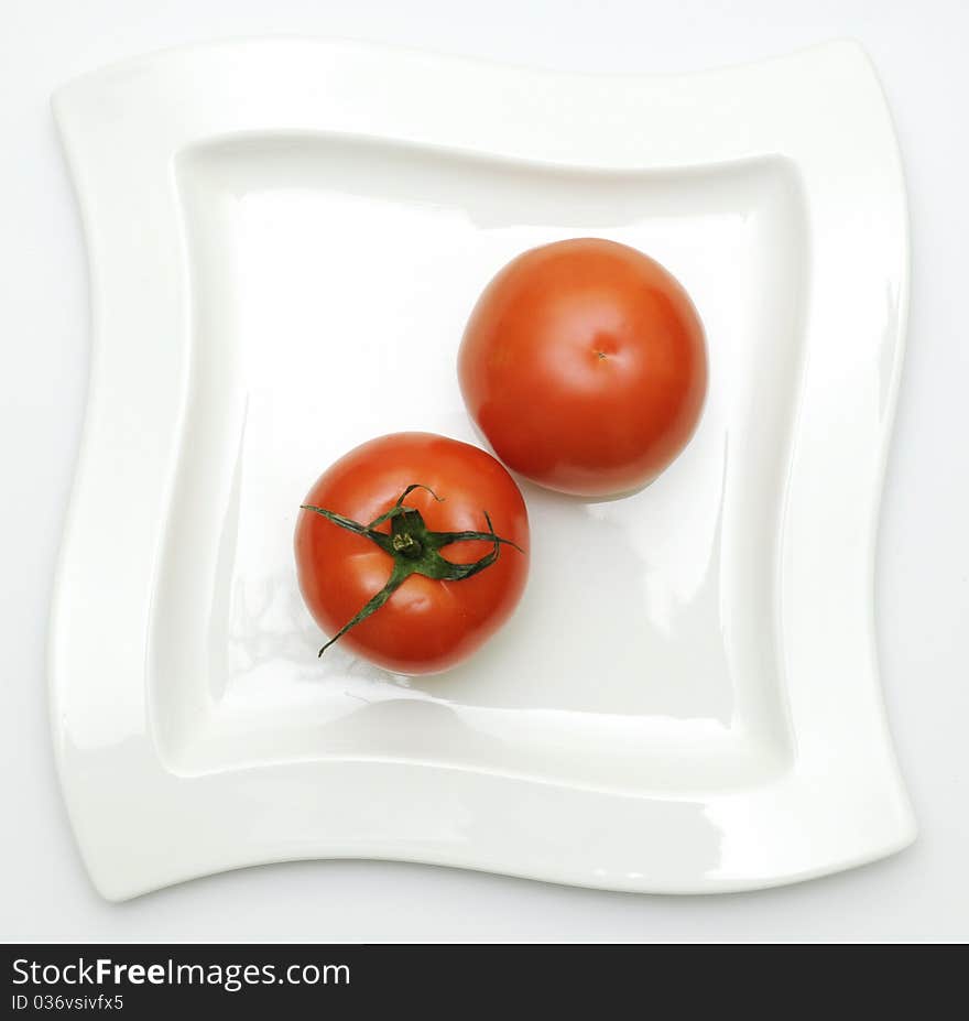 Two tomatoes on white plate-top view. Two tomatoes on white plate-top view.