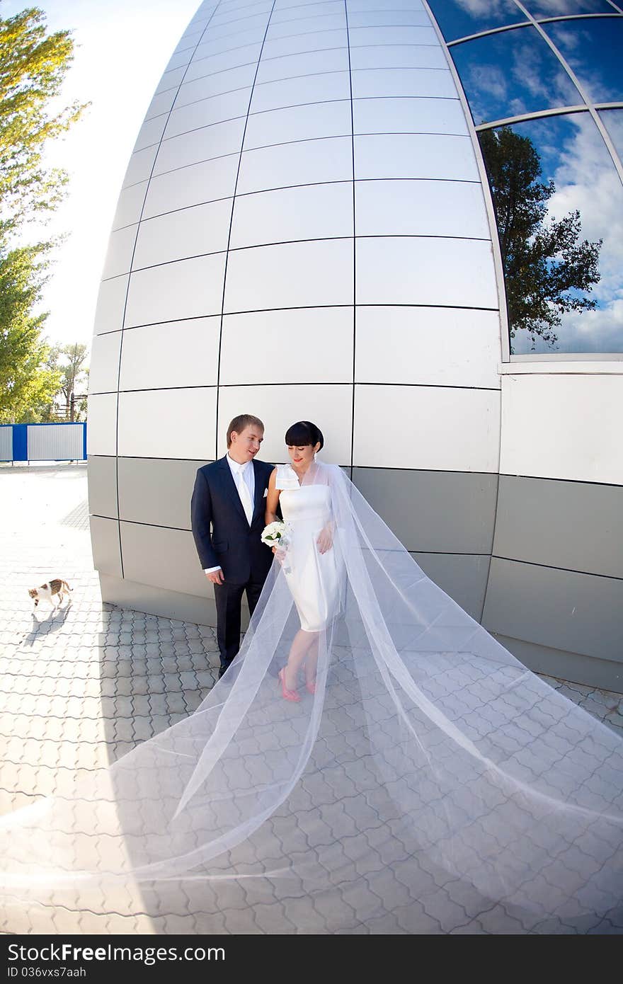 Bride and groom by the wall with long flying veil