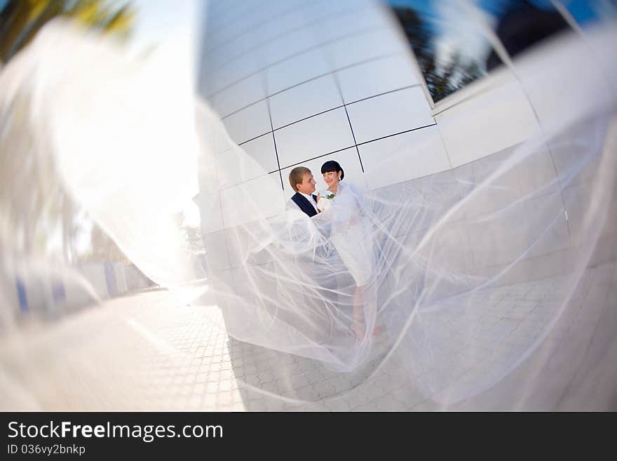 Bride and groom by the wall with long flying veil