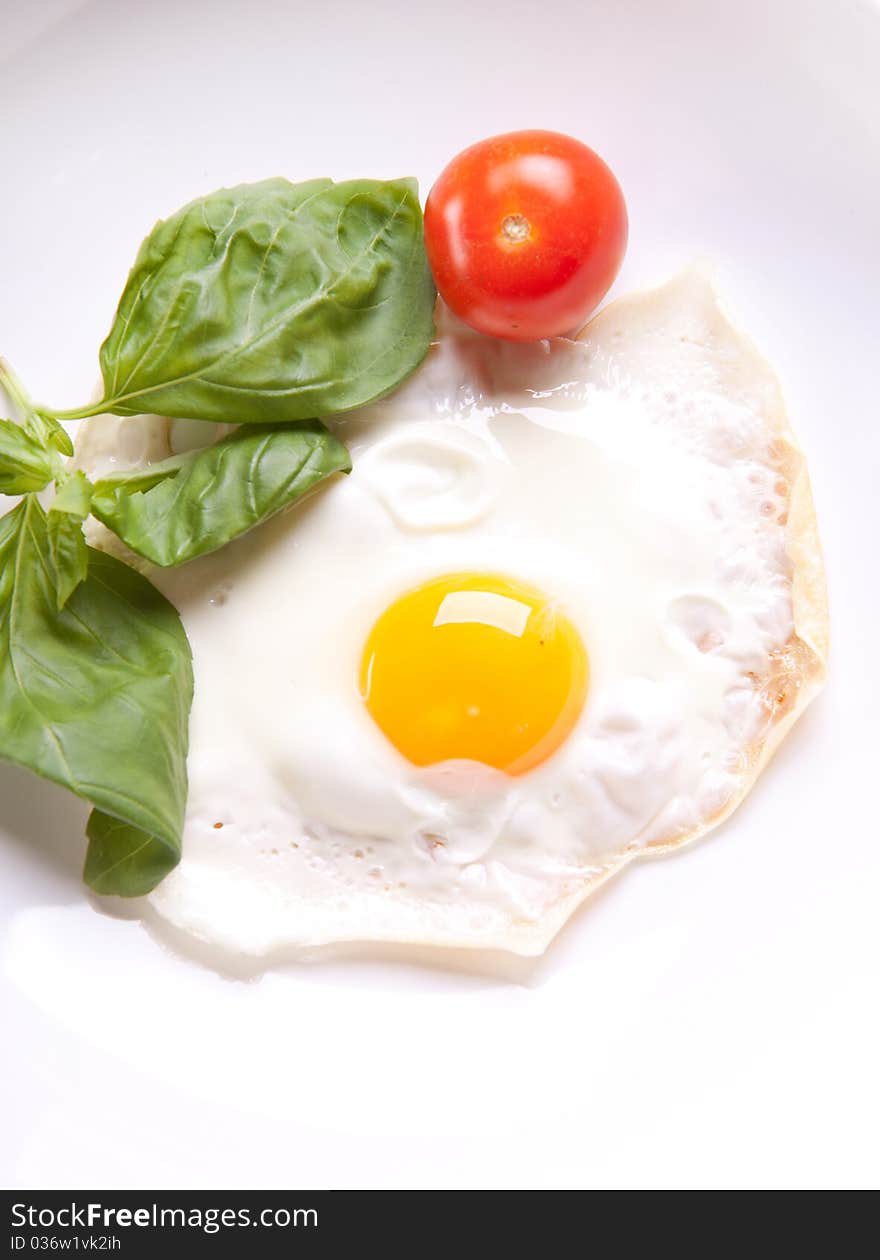 Fried egg served on a white plate with tomato and fresh herbs. Fried egg served on a white plate with tomato and fresh herbs