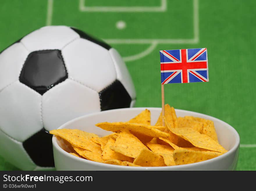 Soccer ball with crispy snacks in a bowl on green background