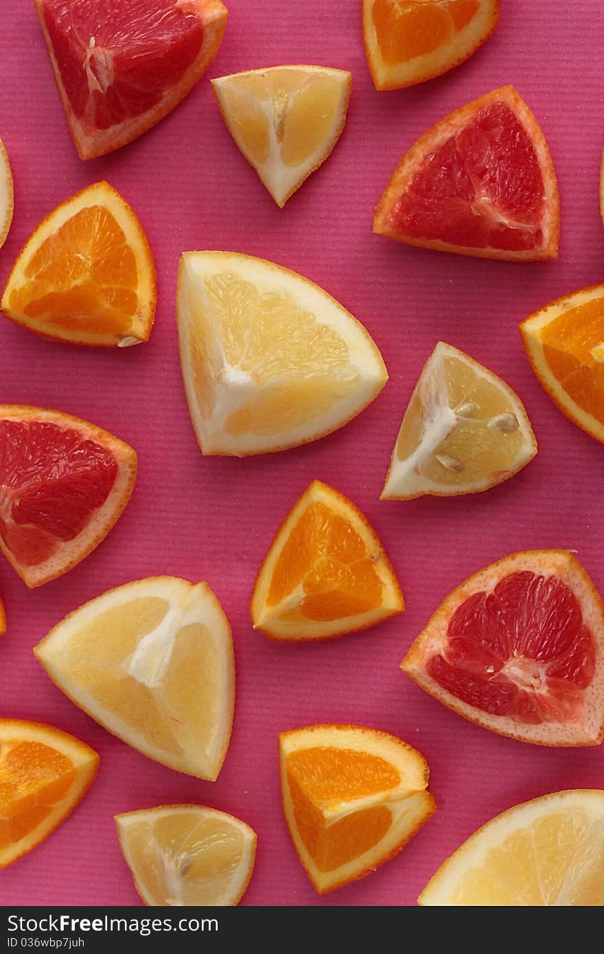 A background of chopped citrus fruits (lemons, oranges, pink & white grapefruit) on pink. A background of chopped citrus fruits (lemons, oranges, pink & white grapefruit) on pink.