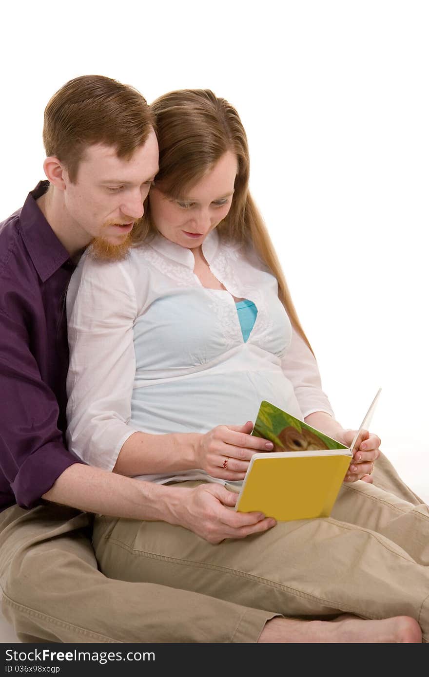 Young couple expecting their first child looking through a childrens book. Young couple expecting their first child looking through a childrens book