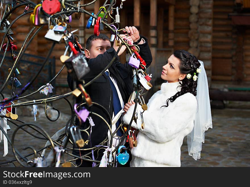 Happy bride and groom near metal tree with symbol lock at a wedding a walk in Moscow. Happy bride and groom near metal tree with symbol lock at a wedding a walk in Moscow