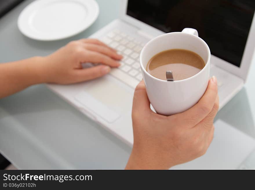 A woman taking a coffee break holding a cup of coffee while working. A woman taking a coffee break holding a cup of coffee while working