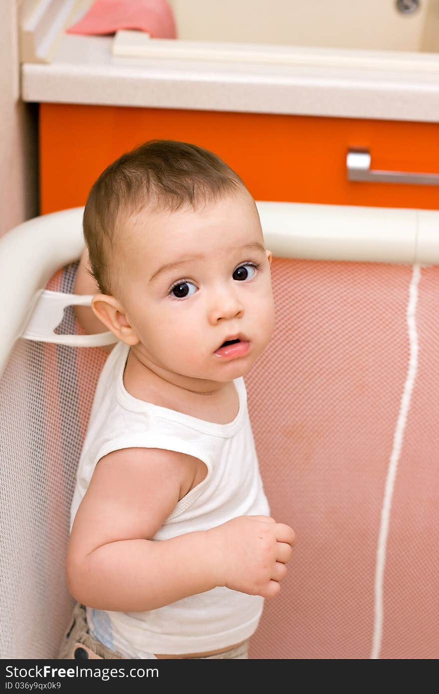 Cute caucasian baby in manege, kitchen housework