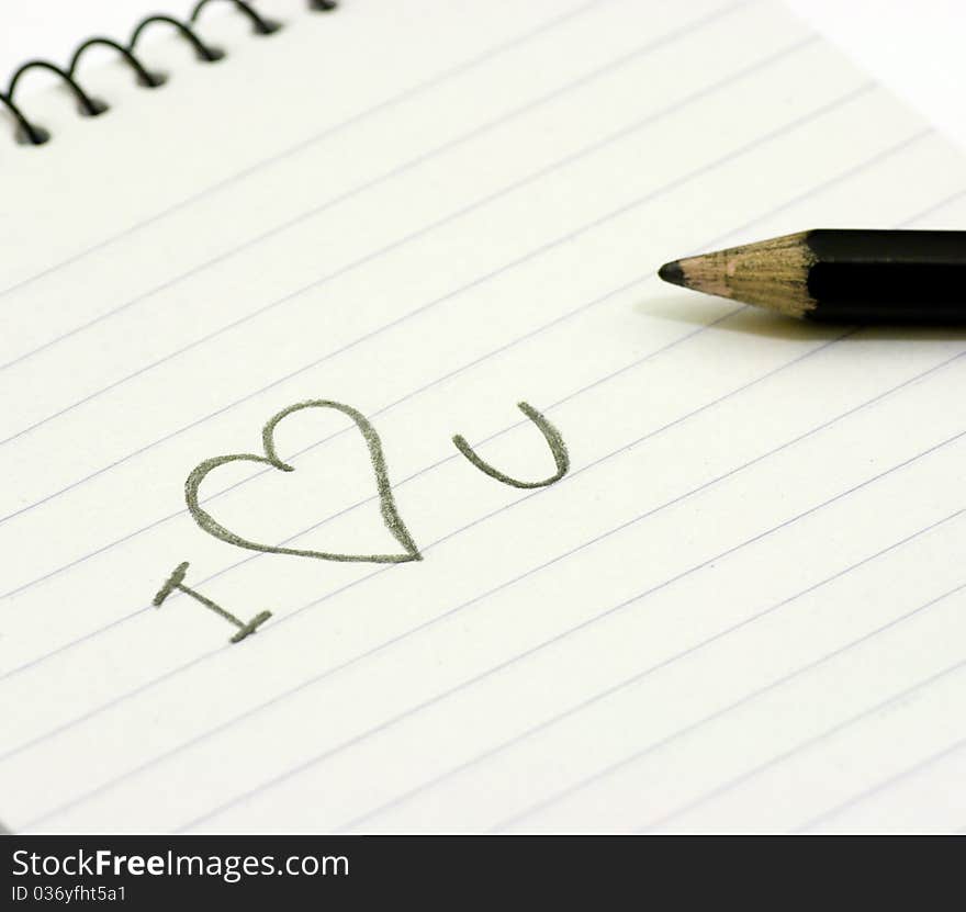 Pencil and small notebook with a love valentine message saying i love you, lying on a white surface