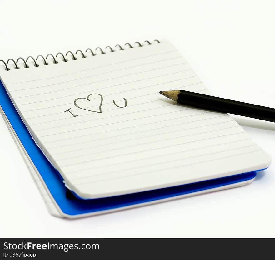 Pencil and small notebook with a love valentine message saying i love you, lying on a white surface