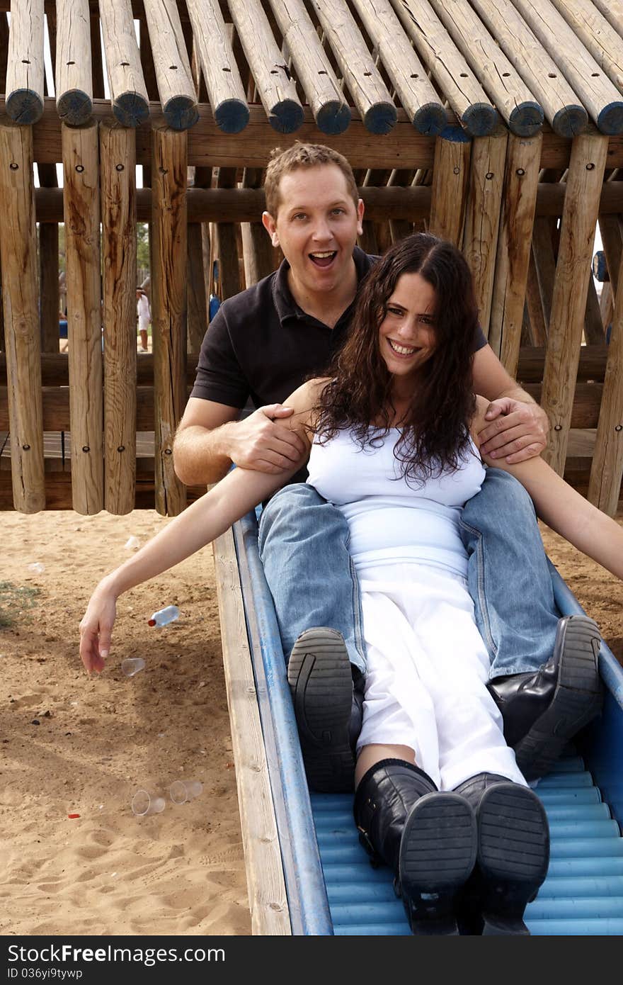 Happy couple sliding on children slide