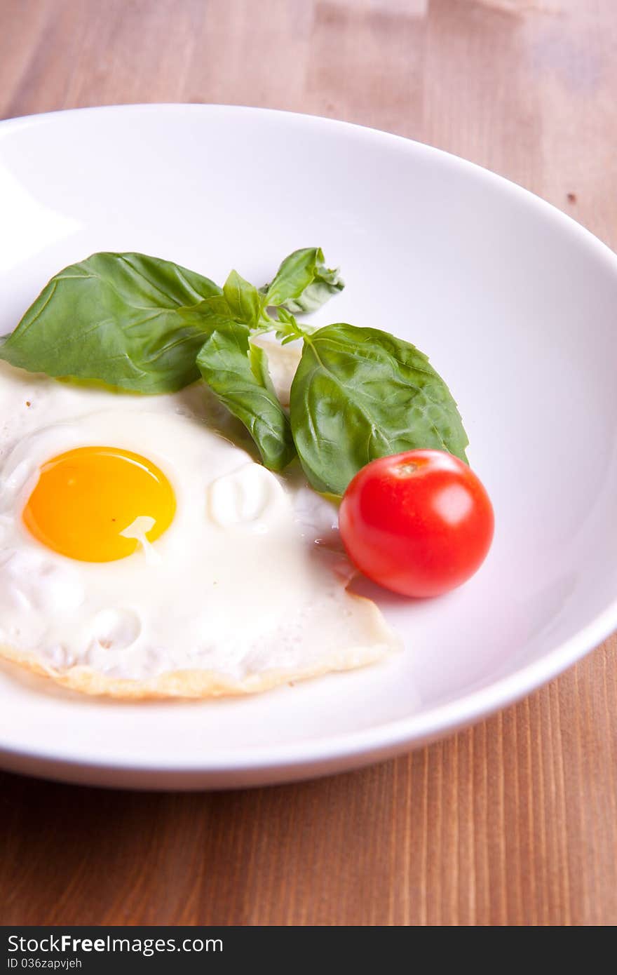 Fried egg served on a white plate with tomato and fresh herbs. Fried egg served on a white plate with tomato and fresh herbs