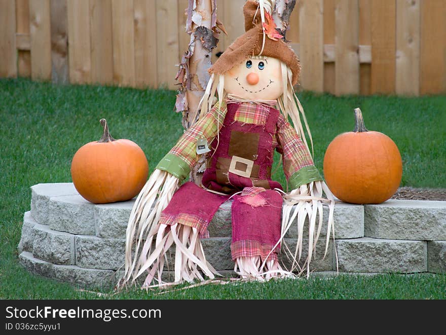 Scarecrow sitting on a brick ledge in the Autumn with two pumpkins. Scarecrow sitting on a brick ledge in the Autumn with two pumpkins.