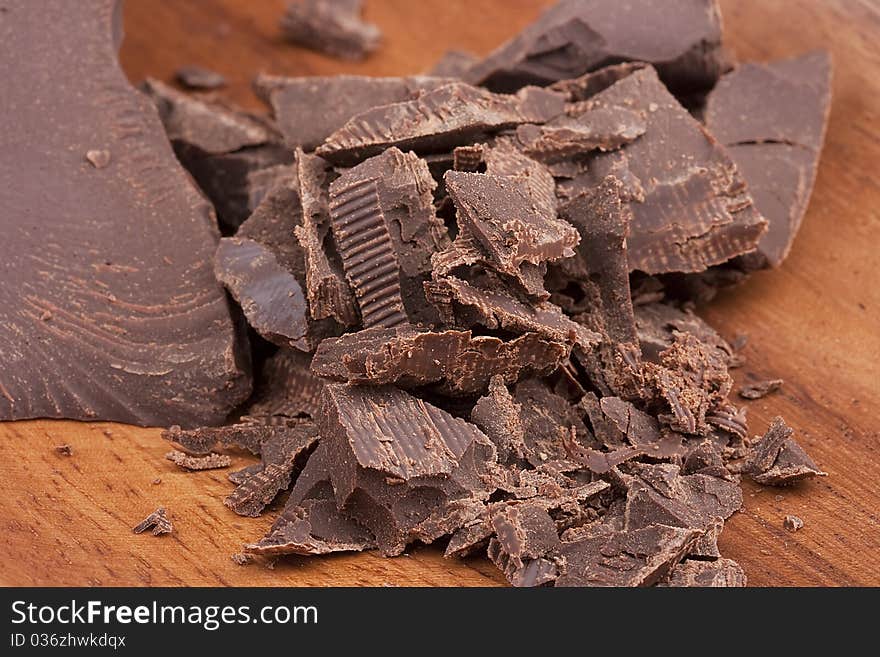 Bitter chocolate in pieces on a brown background in a plate.