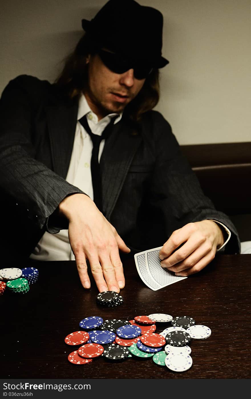 Man with hat and glasses playing underground poker.