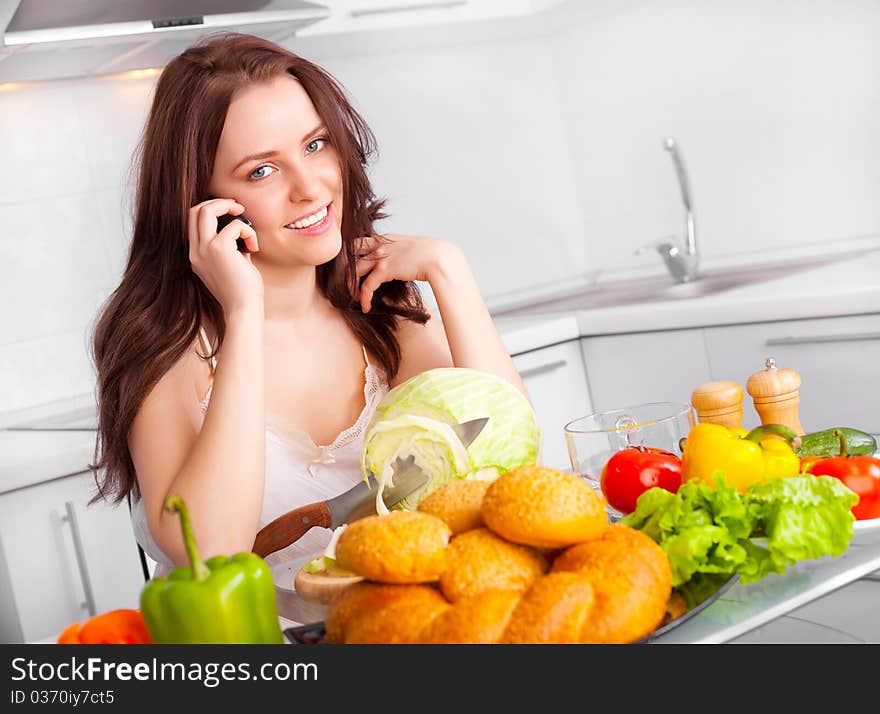 Beautiful young woman cooking in the kitchen and talking on the phone