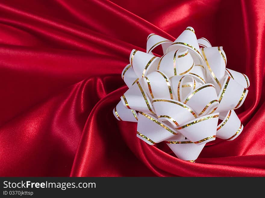 White gift bow on an elegance red silk background. White gift bow on an elegance red silk background