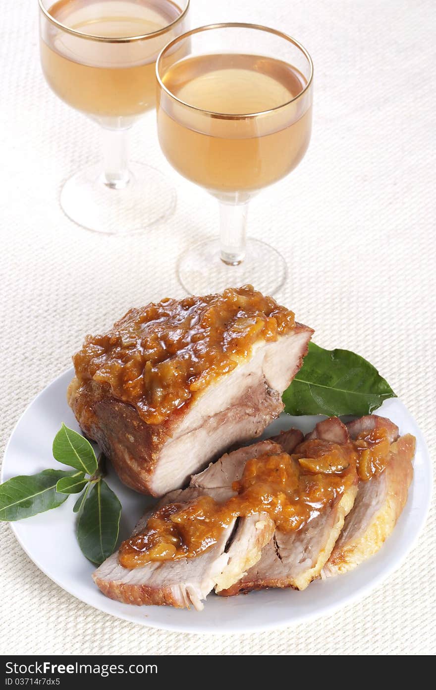 Roasted pork with apricot sauce on a plate and two glasses of wine