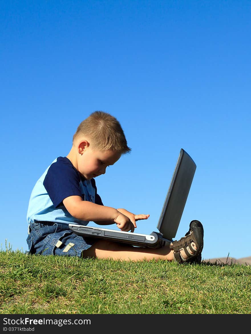 Little boy playing with laptop against blue sky. Little boy playing with laptop against blue sky