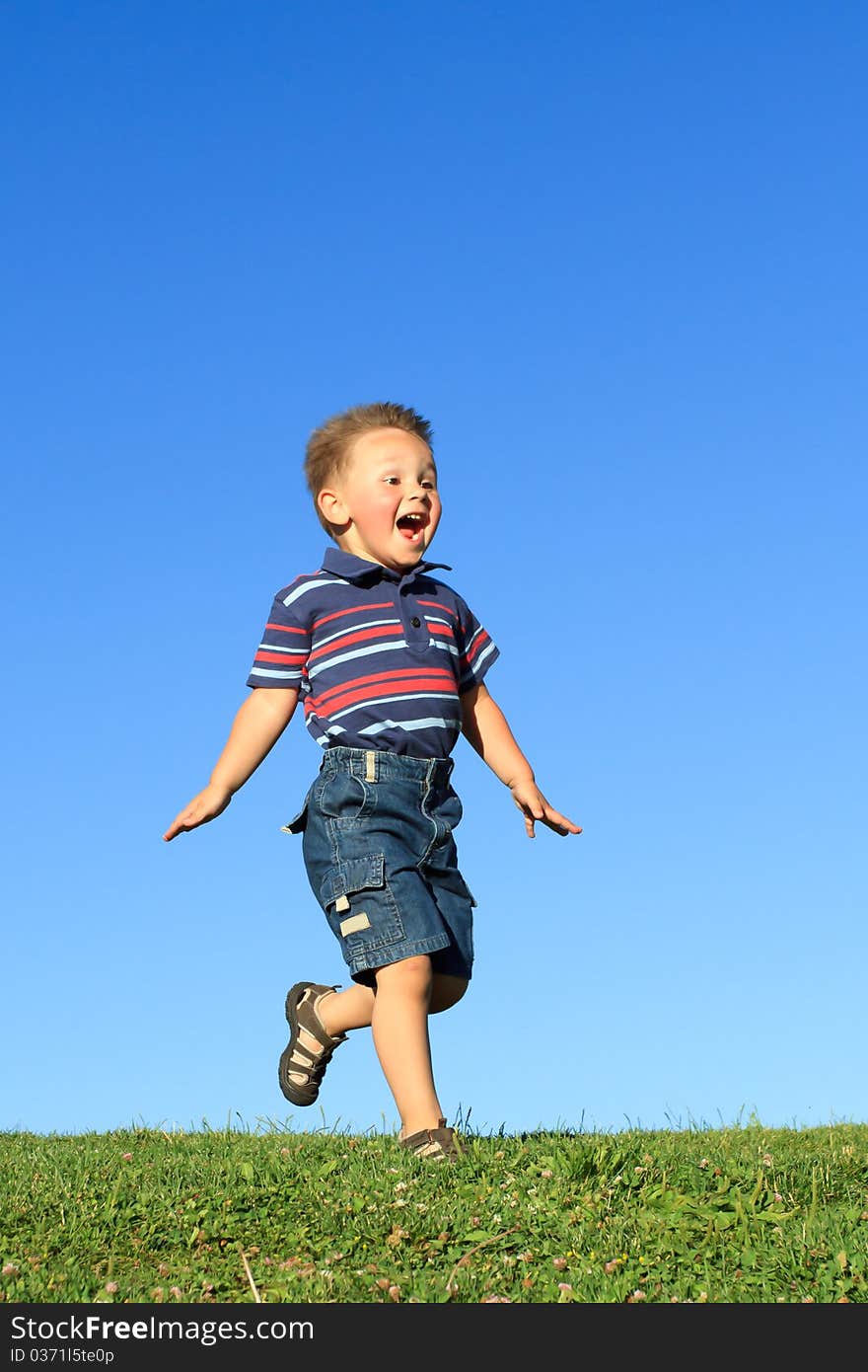 Happy boy running  across hill against blue sky. Happy boy running  across hill against blue sky